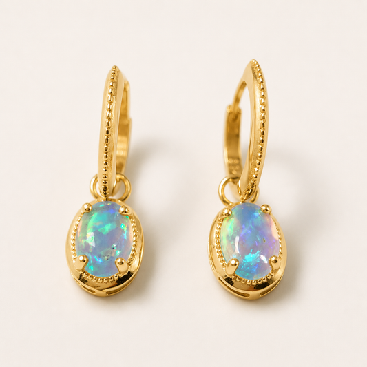 A pair of gold huggie hoop earrings with oval iridescent opal gemstones, displayed on a clean off-white background.
