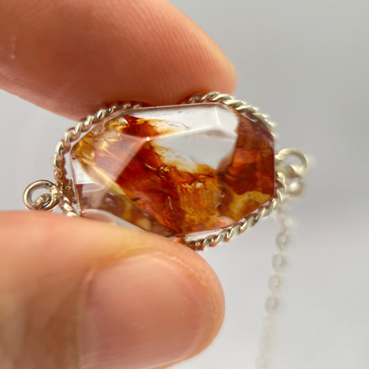 Amber stone pendant held between fingers against a light background
