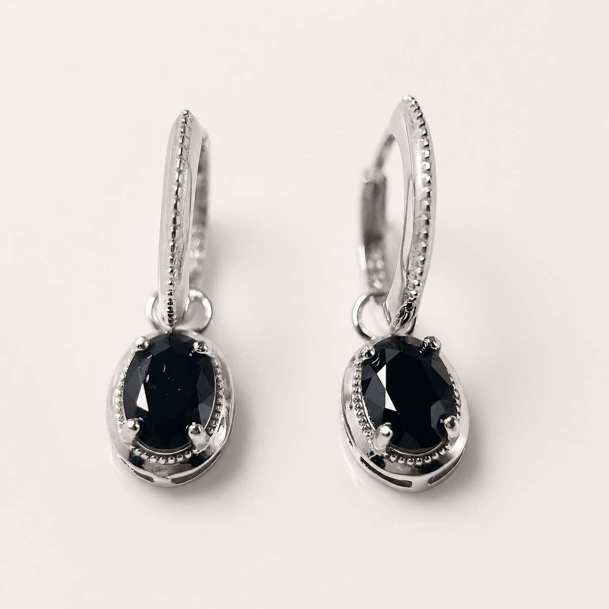A pair of silver huggie hoop earrings with oval black gemstones, shown on a clean off-white background.