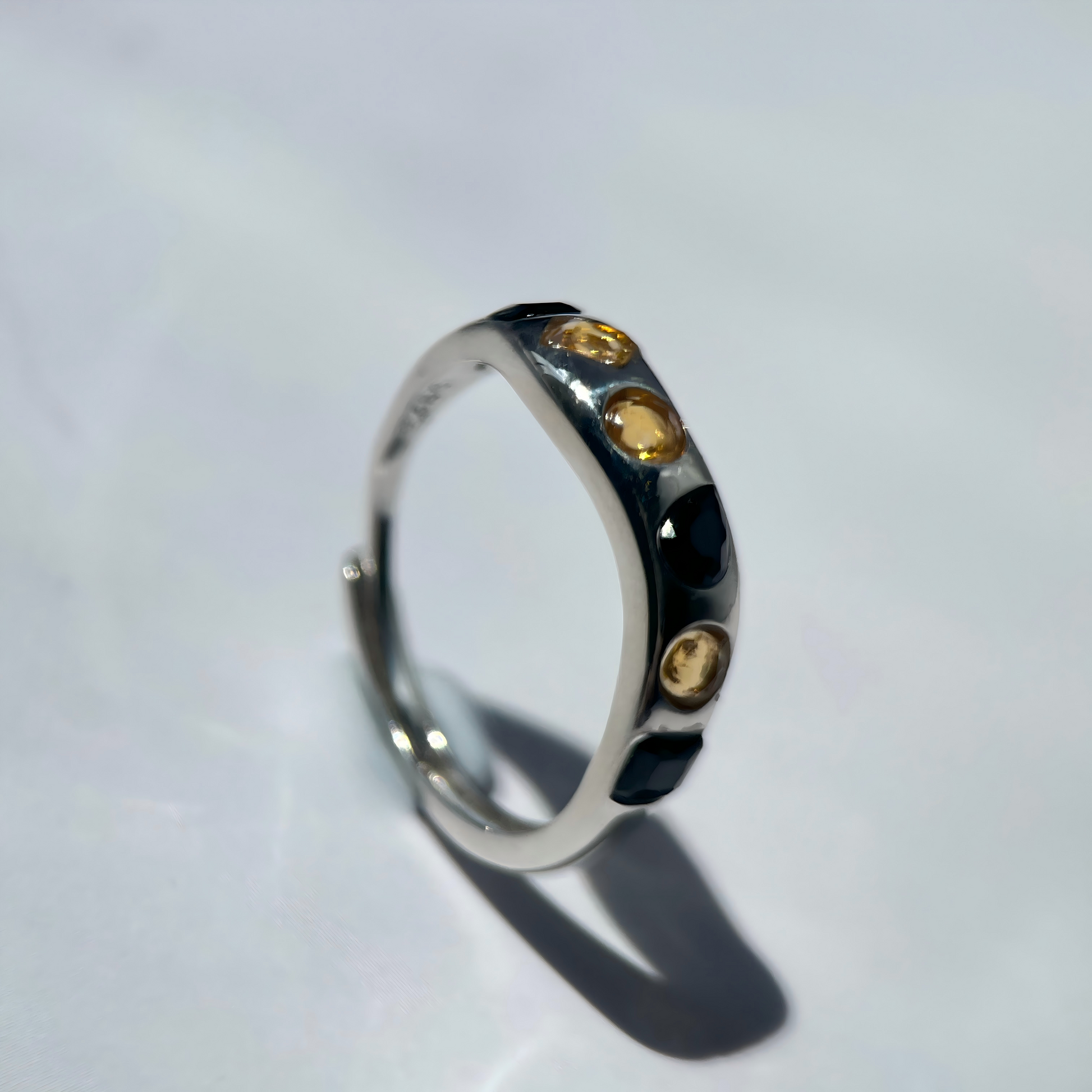 Silver ring with embedded yellow gemstones on a light gray background