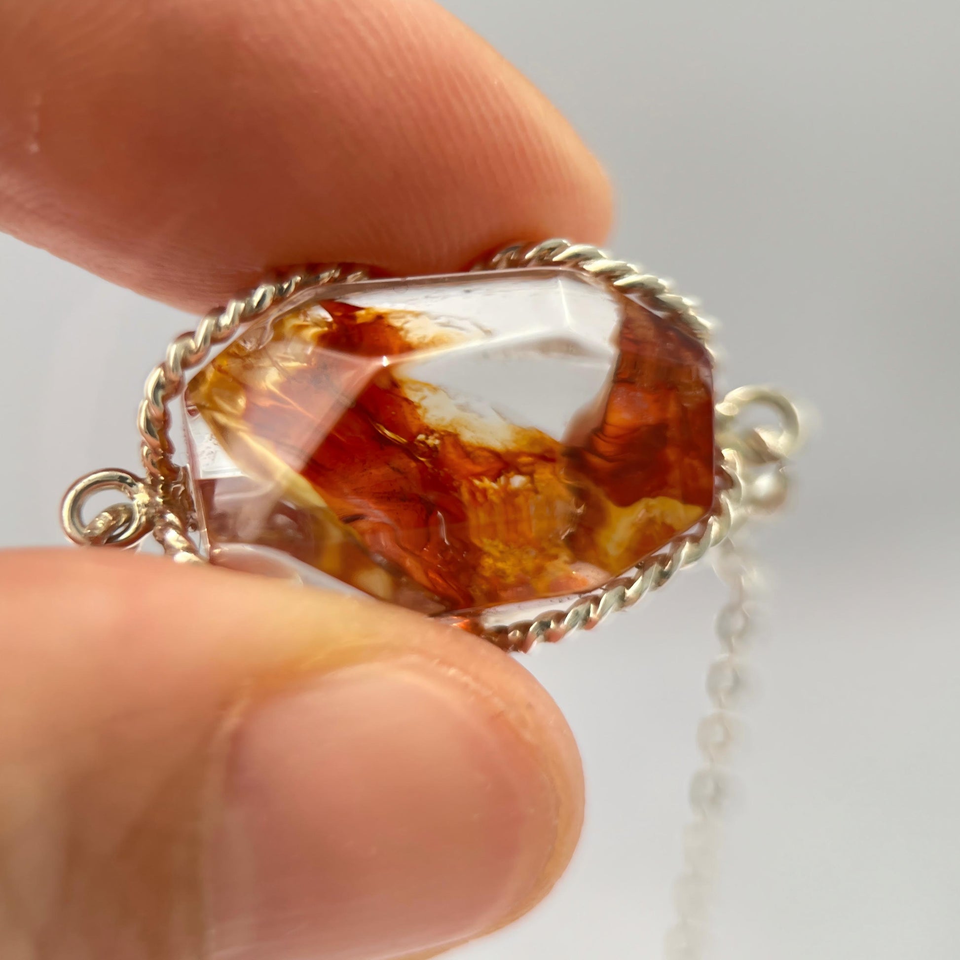 Amber stone pendant held between fingers against a light background