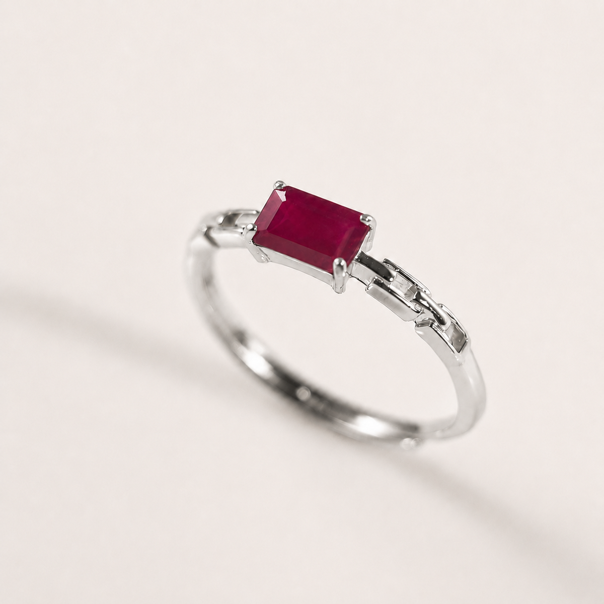 A silver ring featuring a rectangular, cushion-cut ruby, set against a plain off-white background.