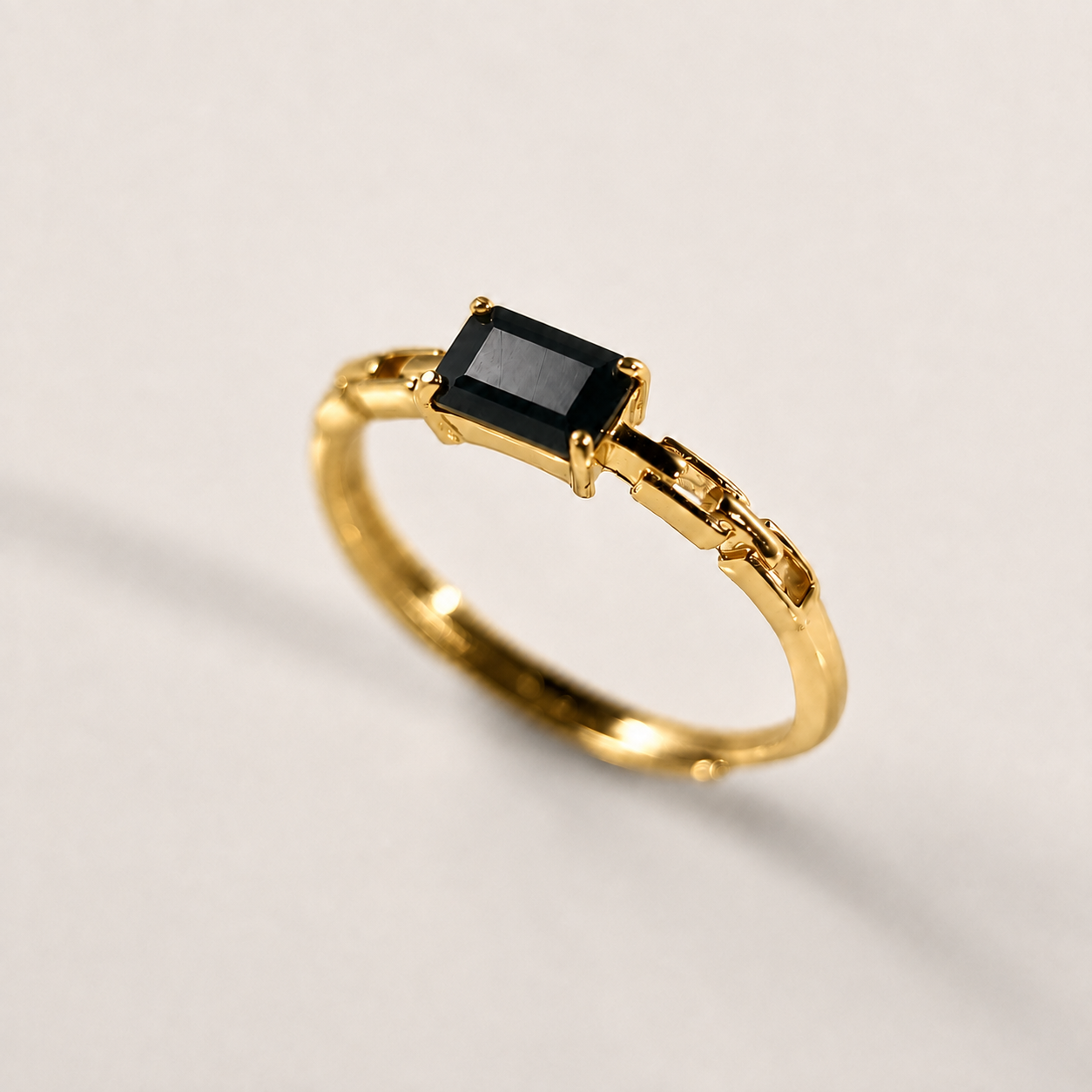 A gold ring featuring a rectangular black gemstone in a prong setting, displayed on a clean, light gray background.