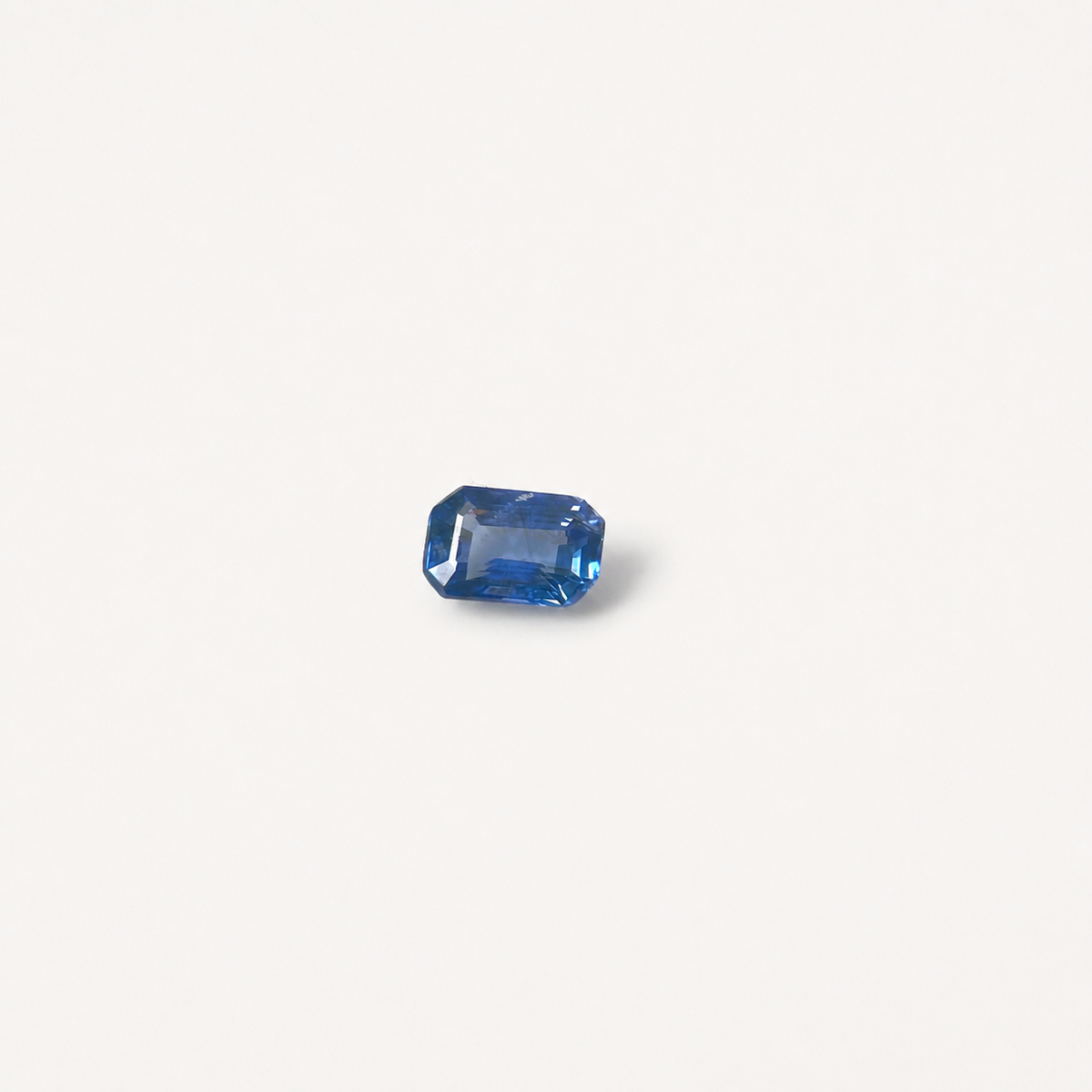 A single rectangular blue gemstone with faceted edges, centered on a plain off-white background.