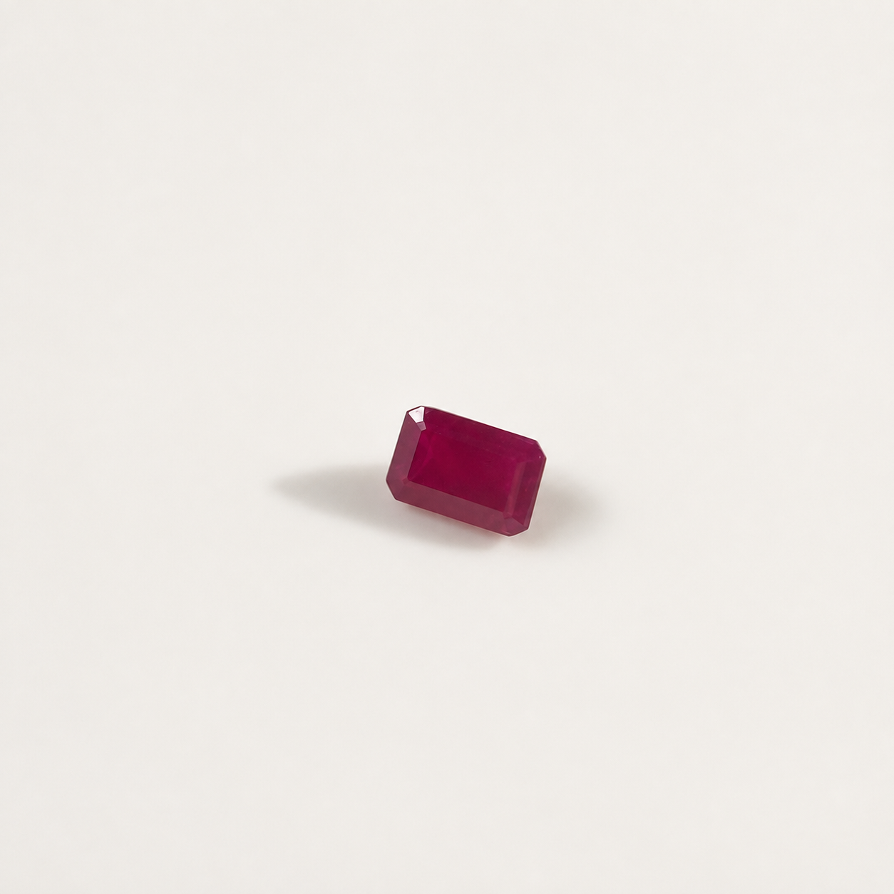 A single rectangular emerald-cut ruby gemstone with faceted edges, displayed on a clean, solid off-white background.