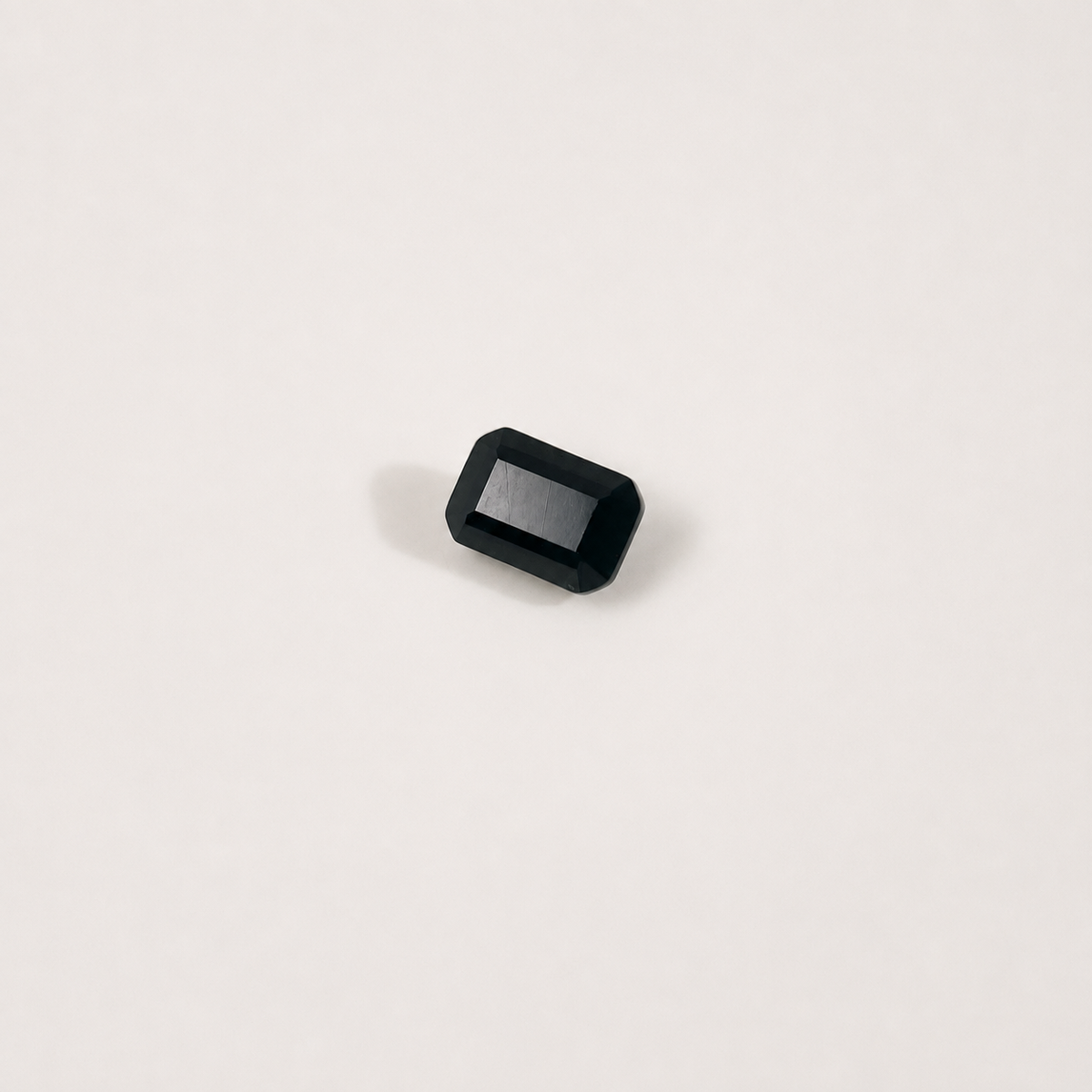 A single rectangular black gemstone with rounded corners and a beveled edge, photographed on a clean off-white background.