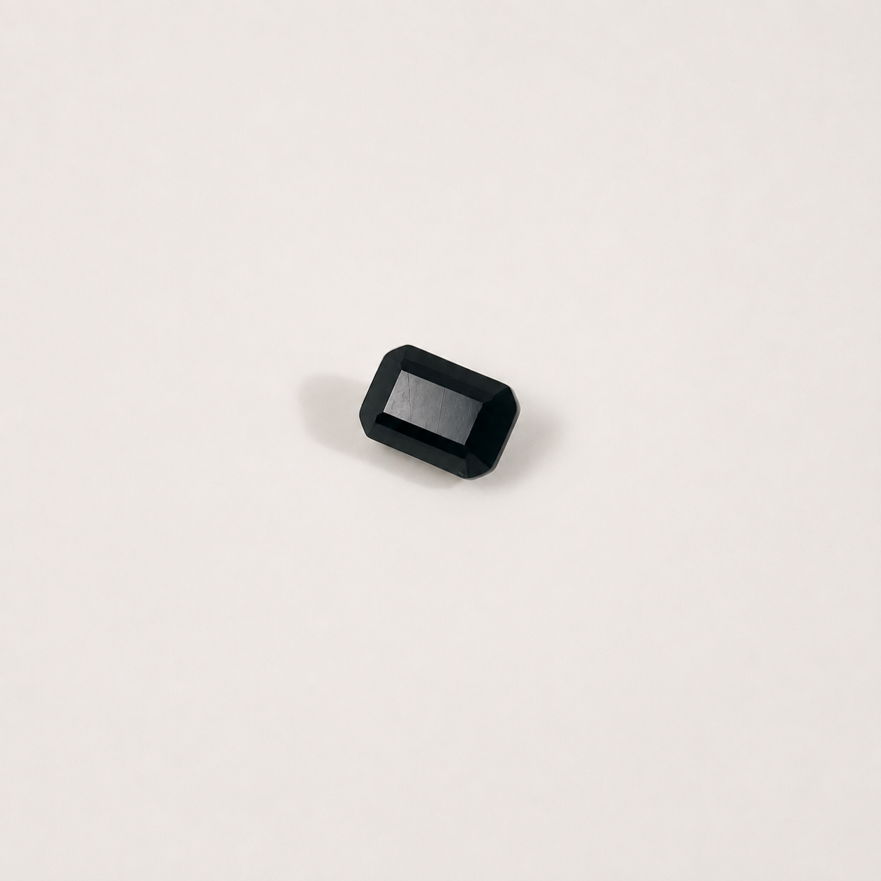 A single rectangular black gemstone with rounded corners and a beveled edge, photographed on a clean off-white background.
