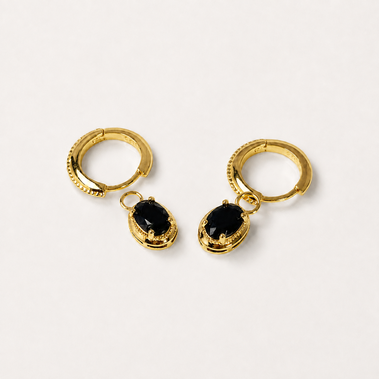 A pair of gold huggie hoop earrings with dangling black faceted marquise-cut gemstones, shown on a clean off-white background.