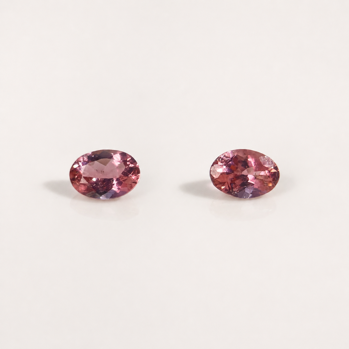 Two oval-cut pink gemstones with a faceted finish, displayed side-by-side on a clean, light off-white background.