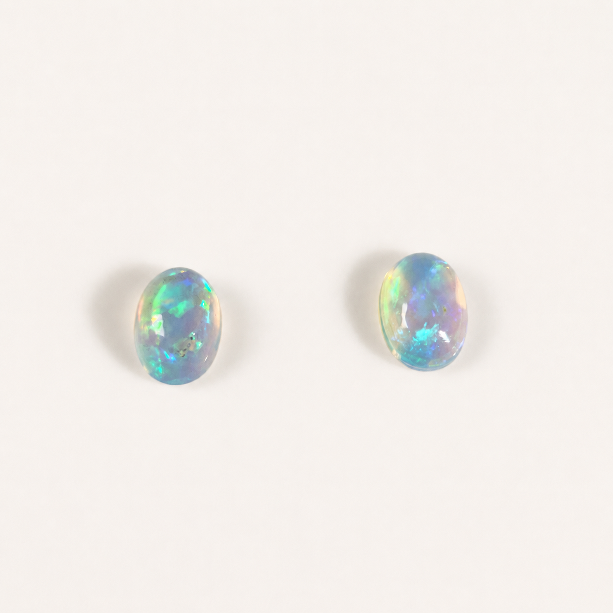 Two oval cabochon opal gemstones with vibrant blue, green, and orange flashes, displayed on a clean off-white background.