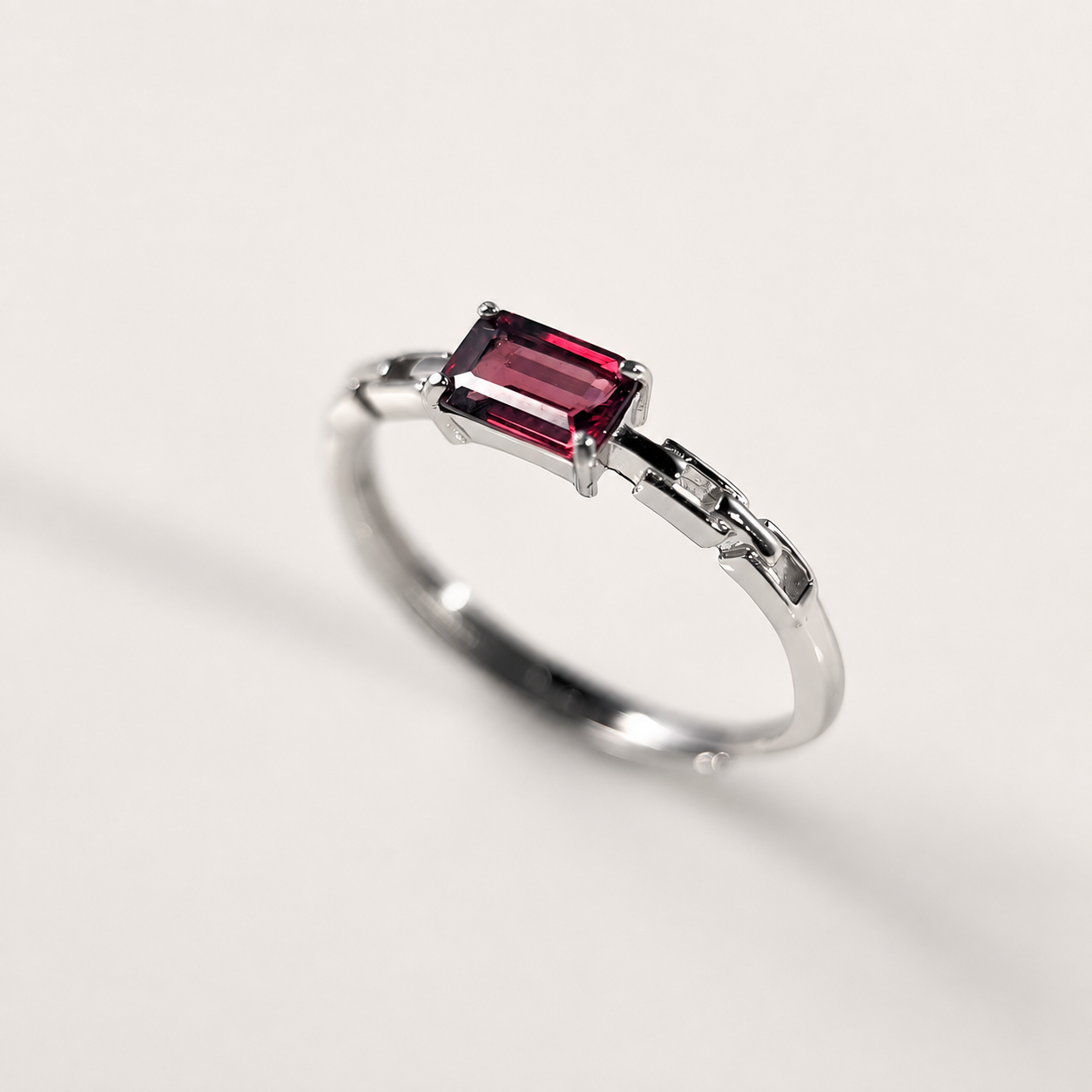 A silver-toned ring featuring a rectangular emerald-cut deep red gemstone, photographed on a clean, light off-white background.