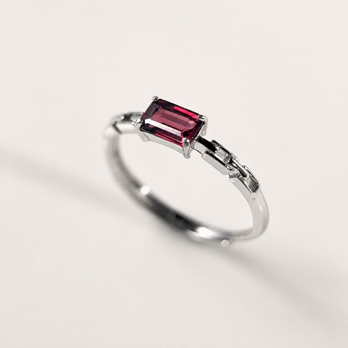 A silver-toned ring featuring a rectangular emerald-cut deep red gemstone, photographed on a clean, light off-white background.