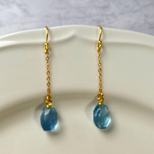Gold earrings with Aquamarine teardrop-shaped beads on a white plate.