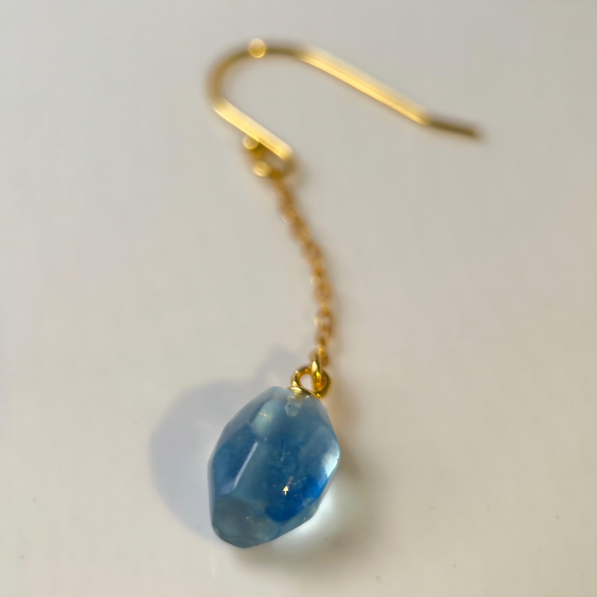 Gold earring with a blue gemstone on a light gray background