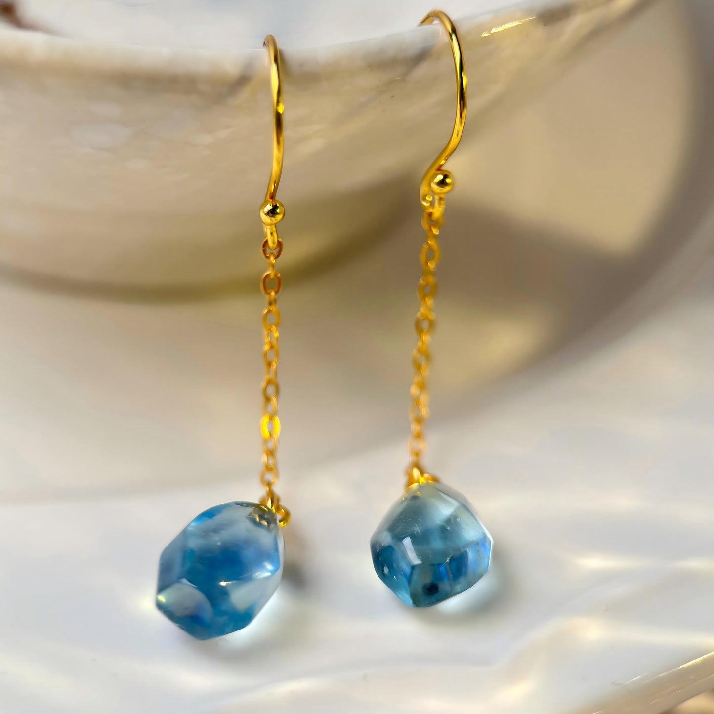 Gold earrings with Aquamarine teardrop beads on a white surface
