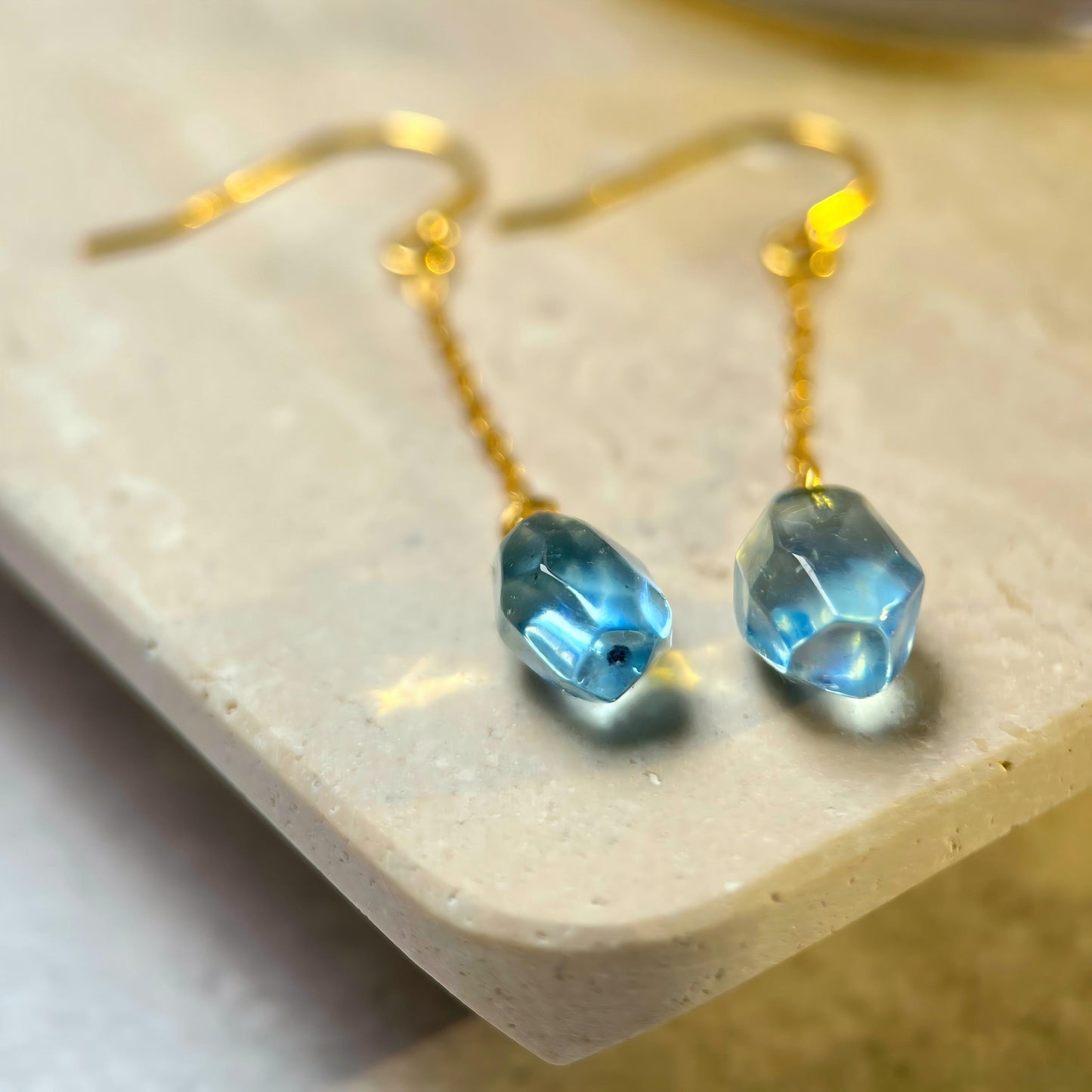 Aquamarine earrings on a beige stone surface