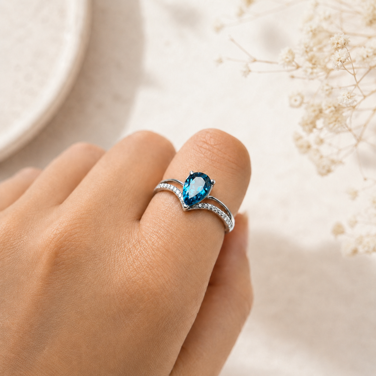 Hand wearing a silver ring with a blue gemstone on a soft background