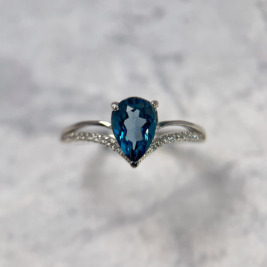 Silver ring with a tear-shaped blue gemstone on a light gray background