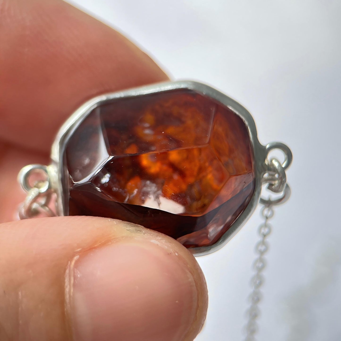 Close-up of a silver pendant with a deep red Hematoid quartz held between fingers against a white background