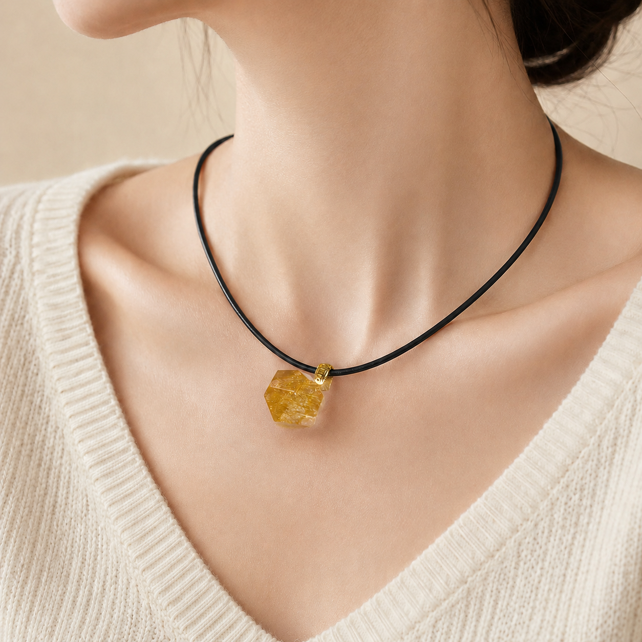 Necklace with a polygonal yellow pendant worn by a person in a beige sweater.