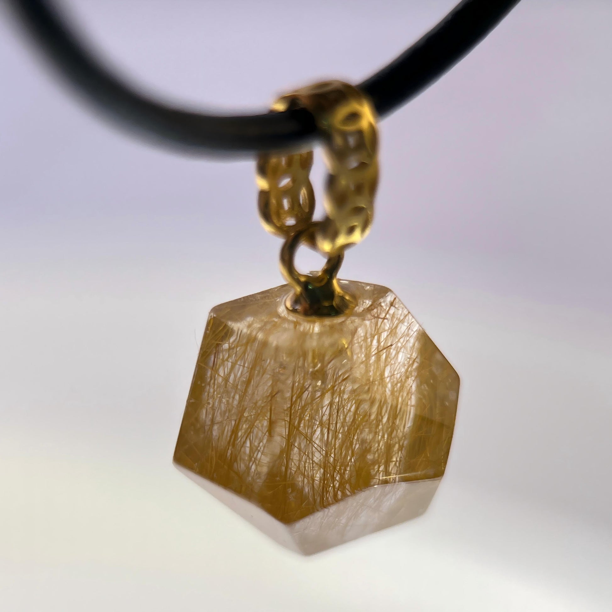 Gold Rutilated Quartz pendant on a black cord against a gradient background