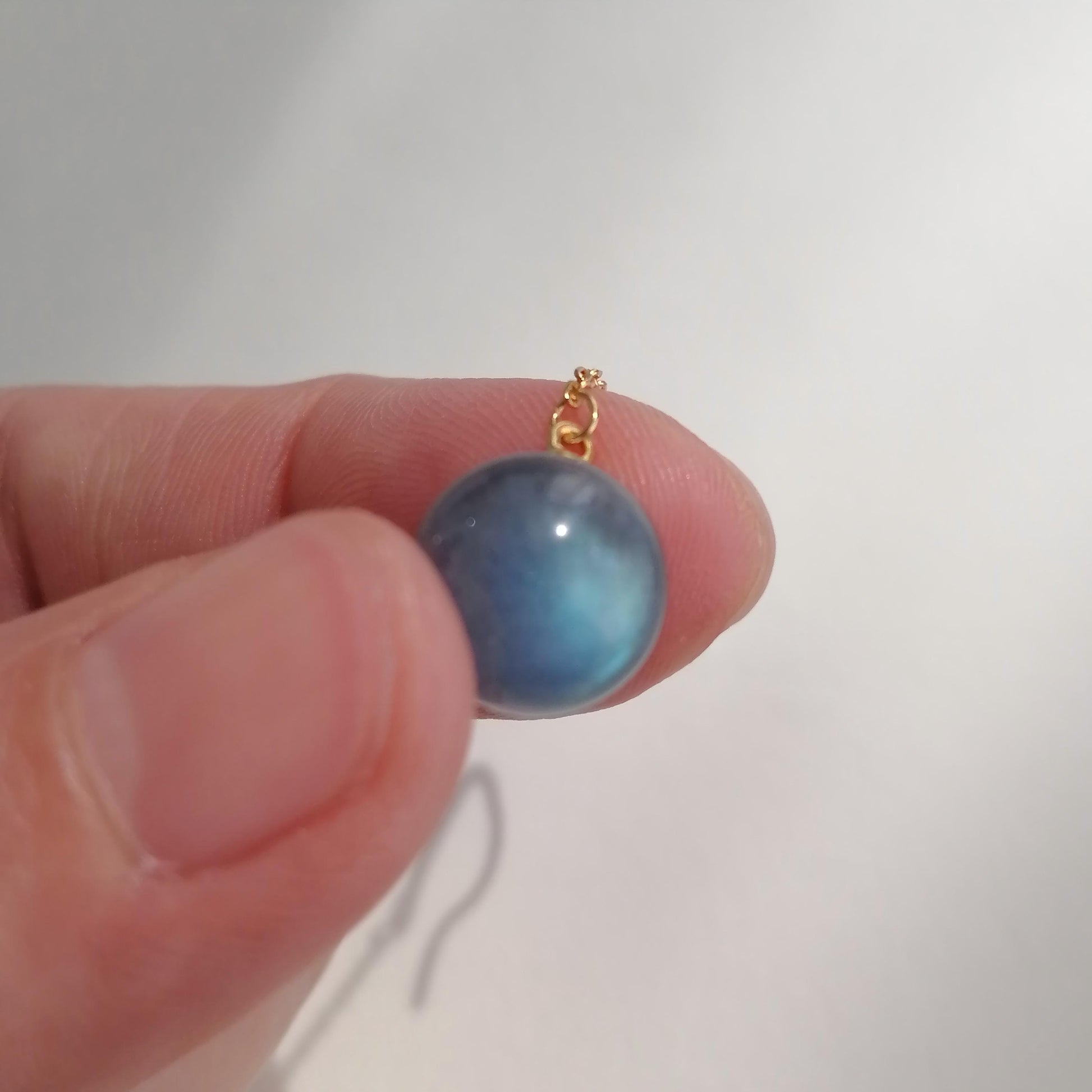 Blue cat's eye gemstone on a gold chain held between fingers against a white background