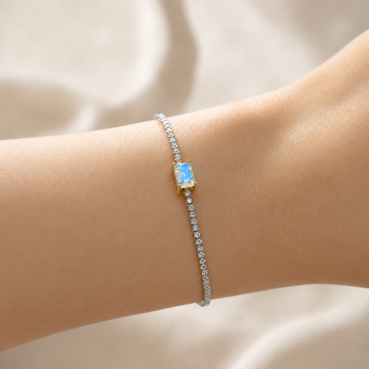 A delicate bracelet worn on a wrist, featuring a central rectangular light blue moonstone in a gold setting, with a silver-toned pavé chain extending downward.