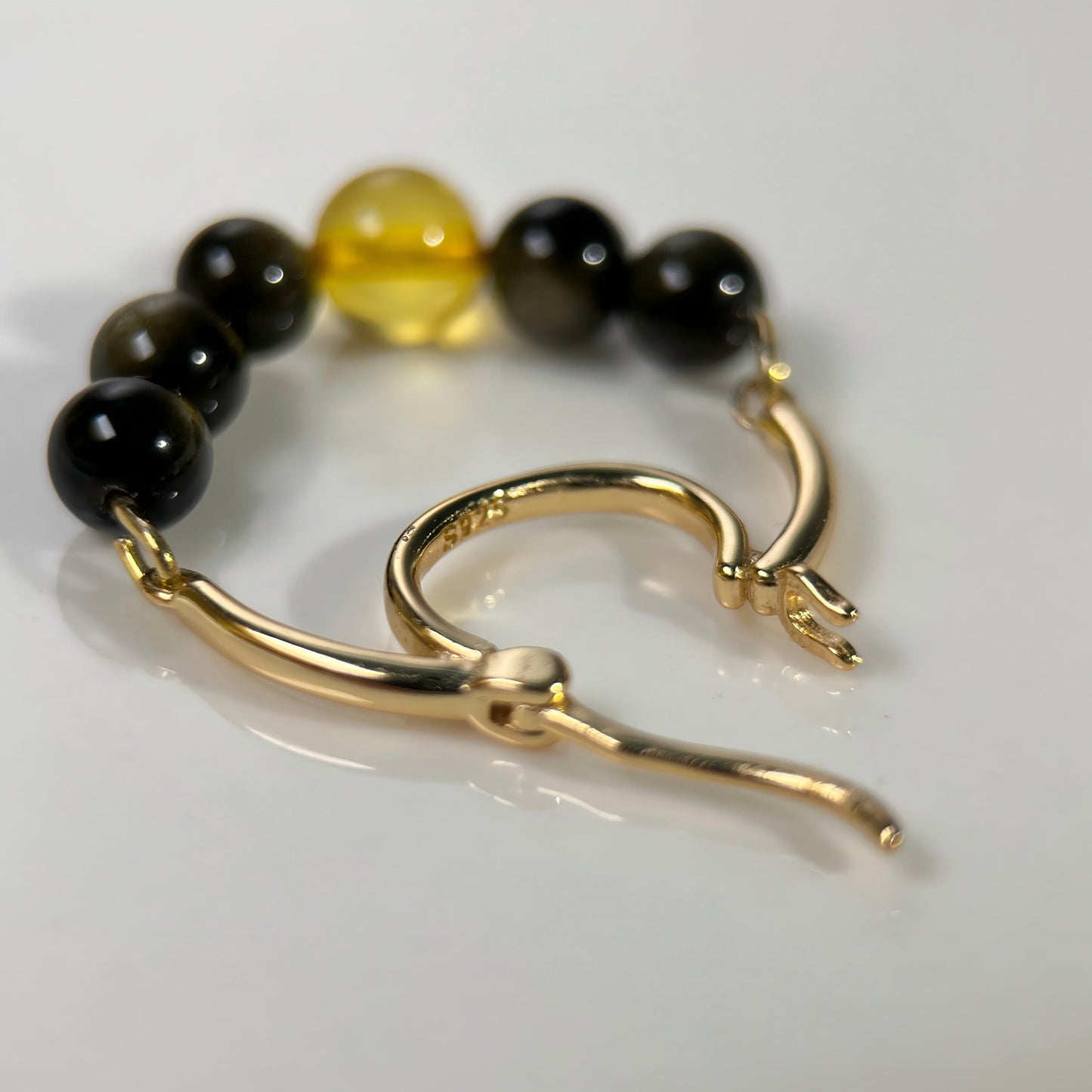 A gold-toned hoop earring with a beaded strand featuring black and translucent amber-yellow beads, photographed on a clean white surface.