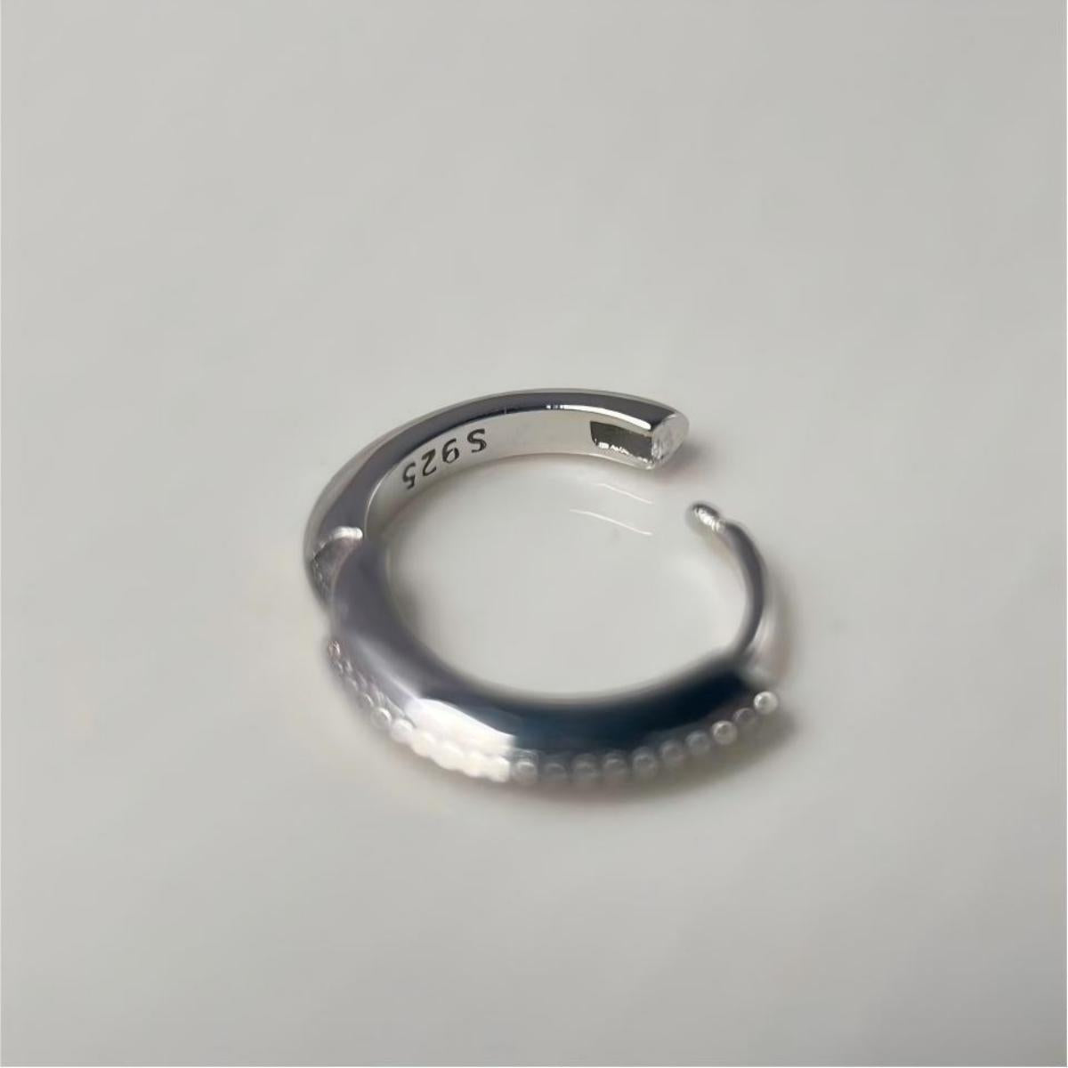A silver-toned open huggie with a textured curve and a polished inner band stamped with 'S925', shown on a plain light gray background.