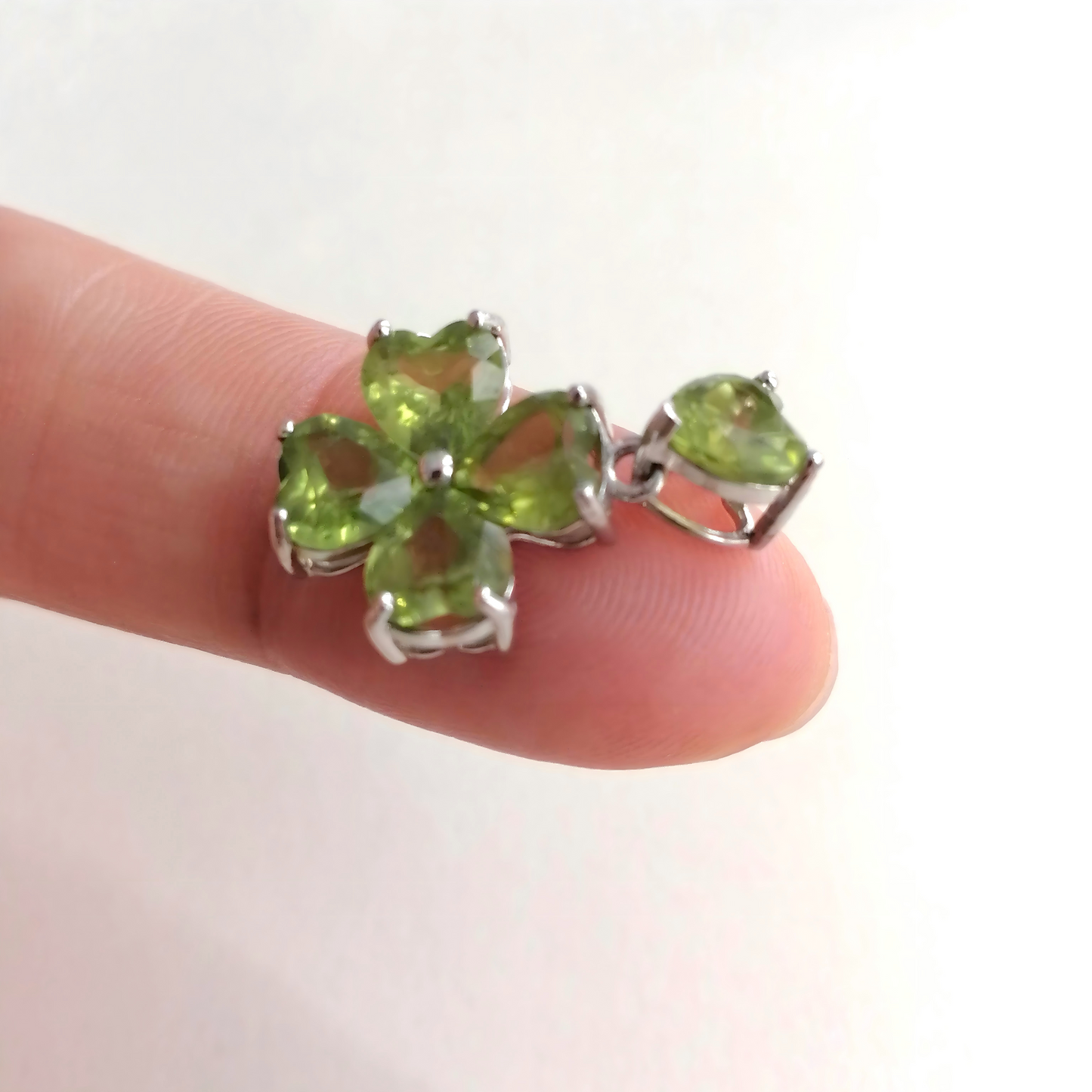 Green gemstone pendant held between fingers against a white background
