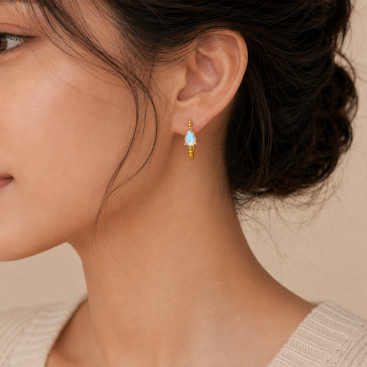 Close-up of a woman wearing a gold earring with a blue gemstone on a beige background