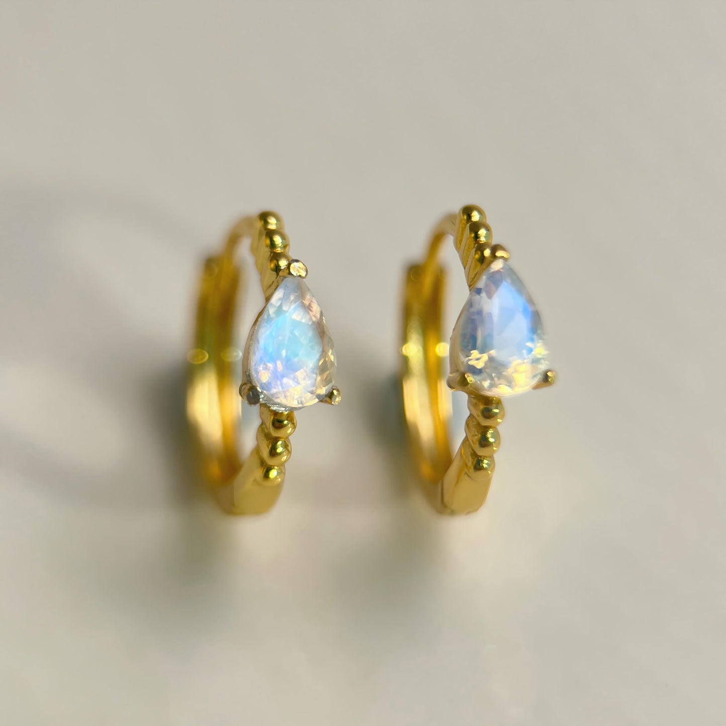 Gold hoop earrings with teardrop-shaped opal stones on a light background
