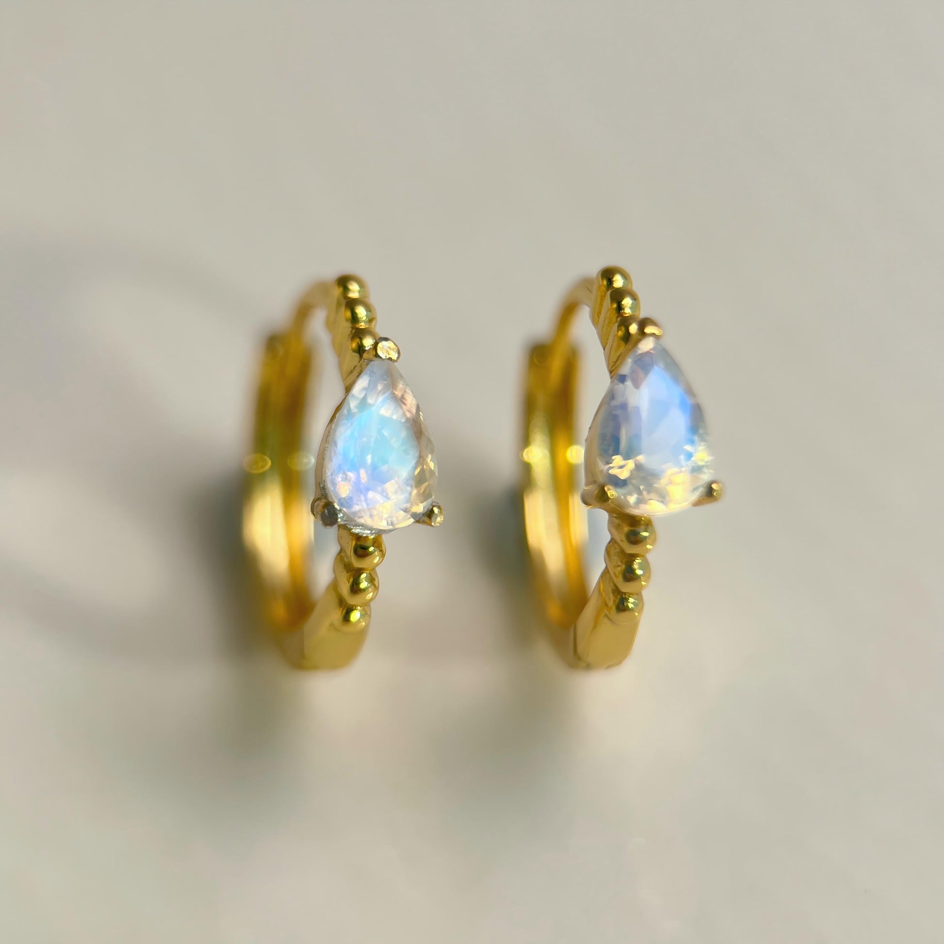 Gold hoop earrings with teardrop-shaped opal stones on a light background