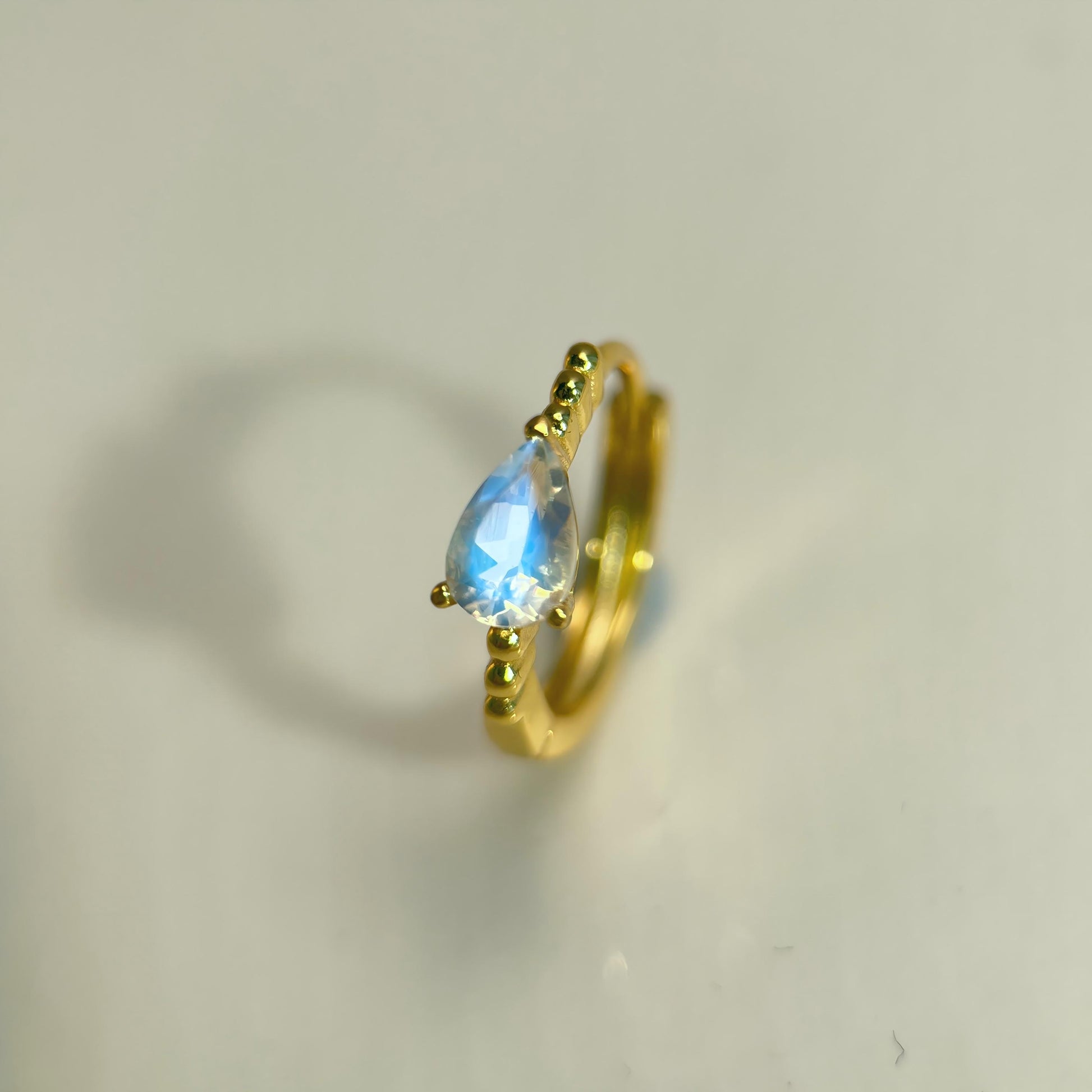 Gold ring with a teardrop-shaped gemstone on a light gray background