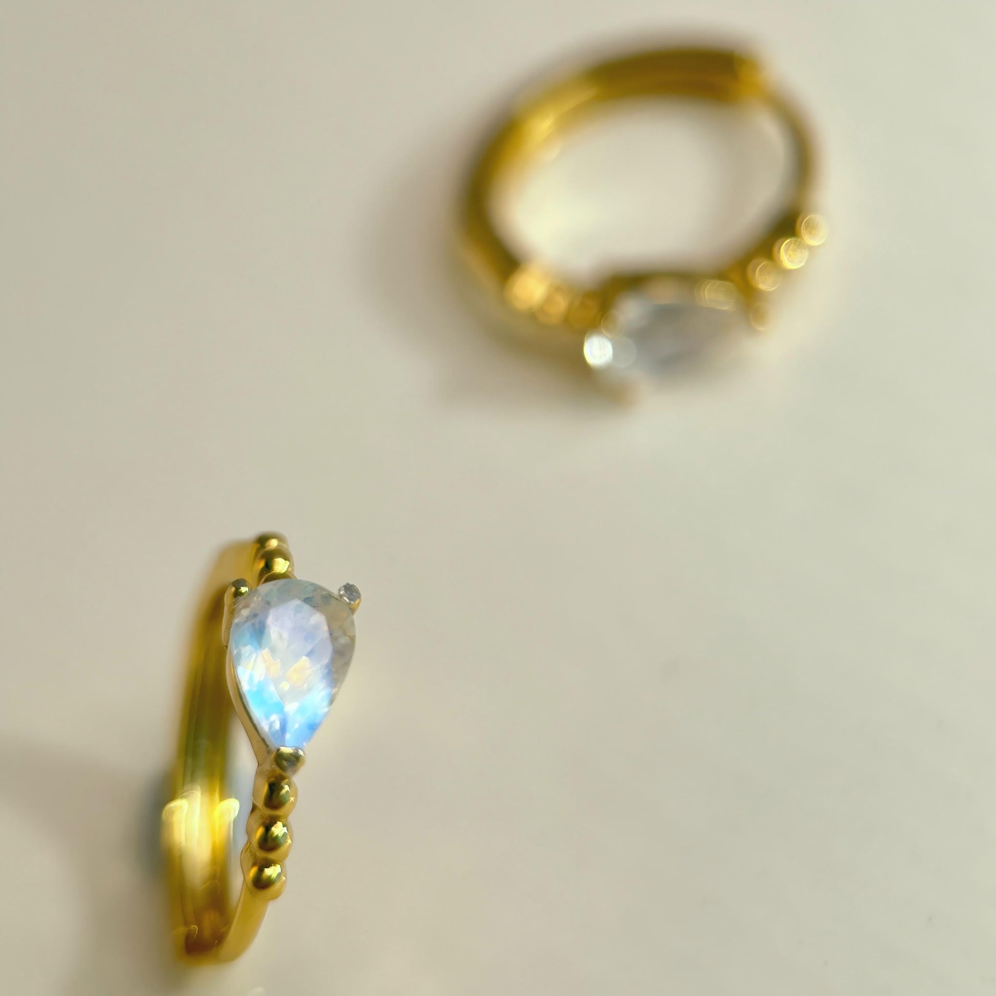 Gold hoop earrings with teardrop-shaped gemstones on a light background