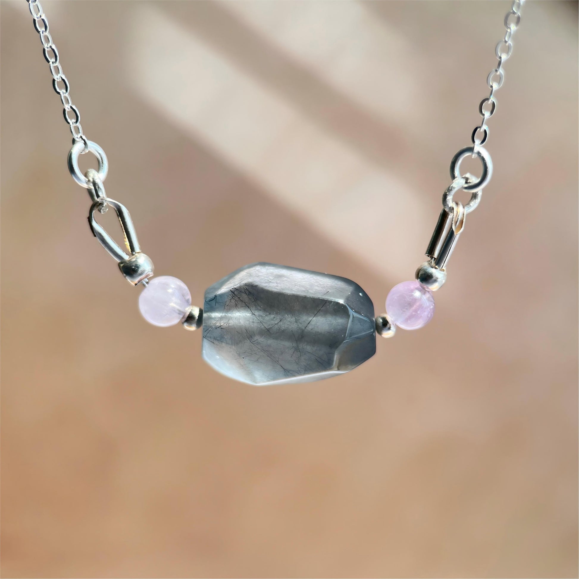 Necklace with a large gray blue stone and smaller purple stones on a blurred background