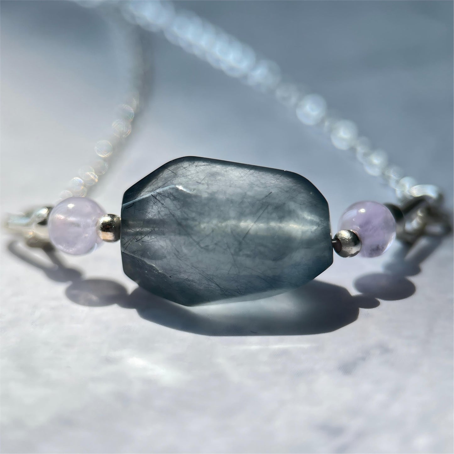 Necklace with a large gray blue bead and smaller purple beads on a light background