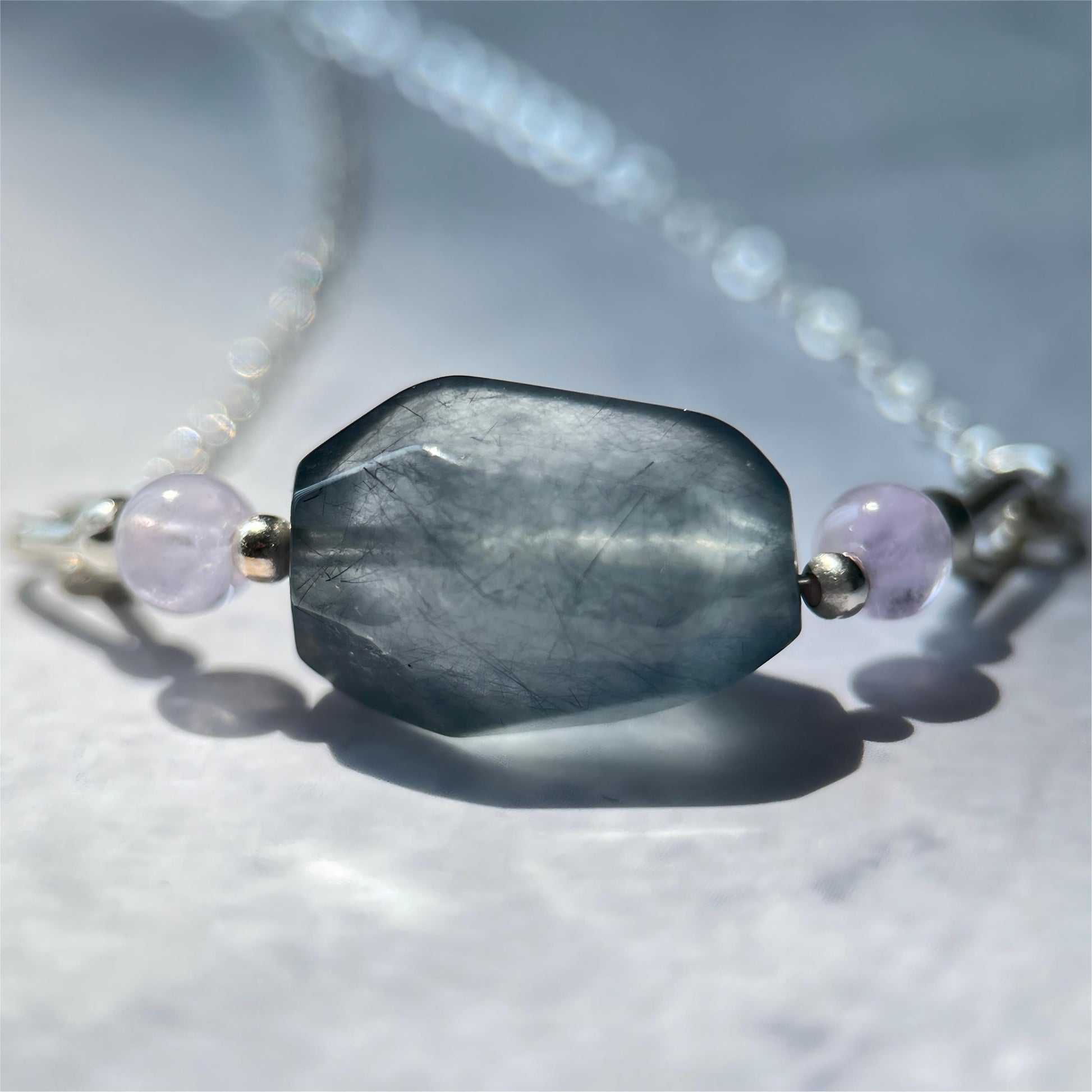 Necklace with a large gray blue bead and smaller purple beads on a light background