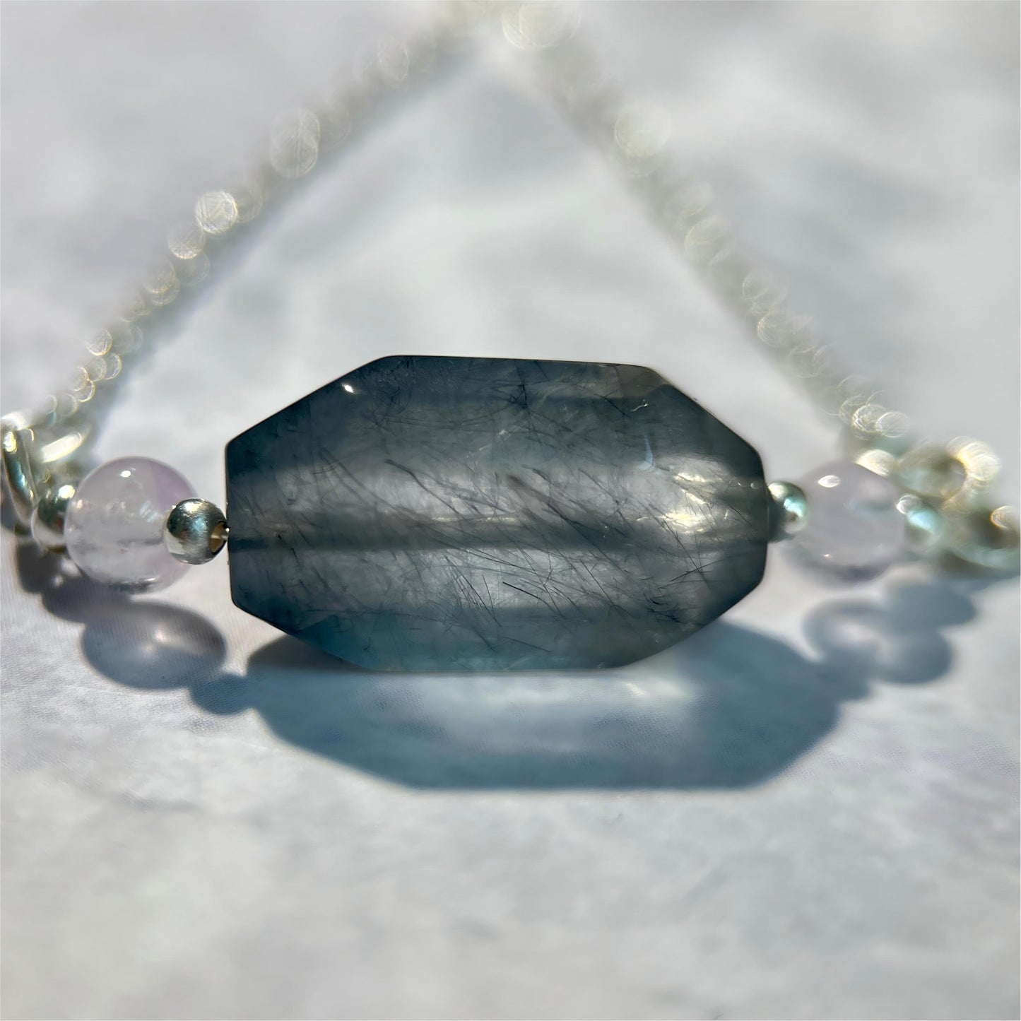 Necklace with a rabbit hair quartz pendant on a light background